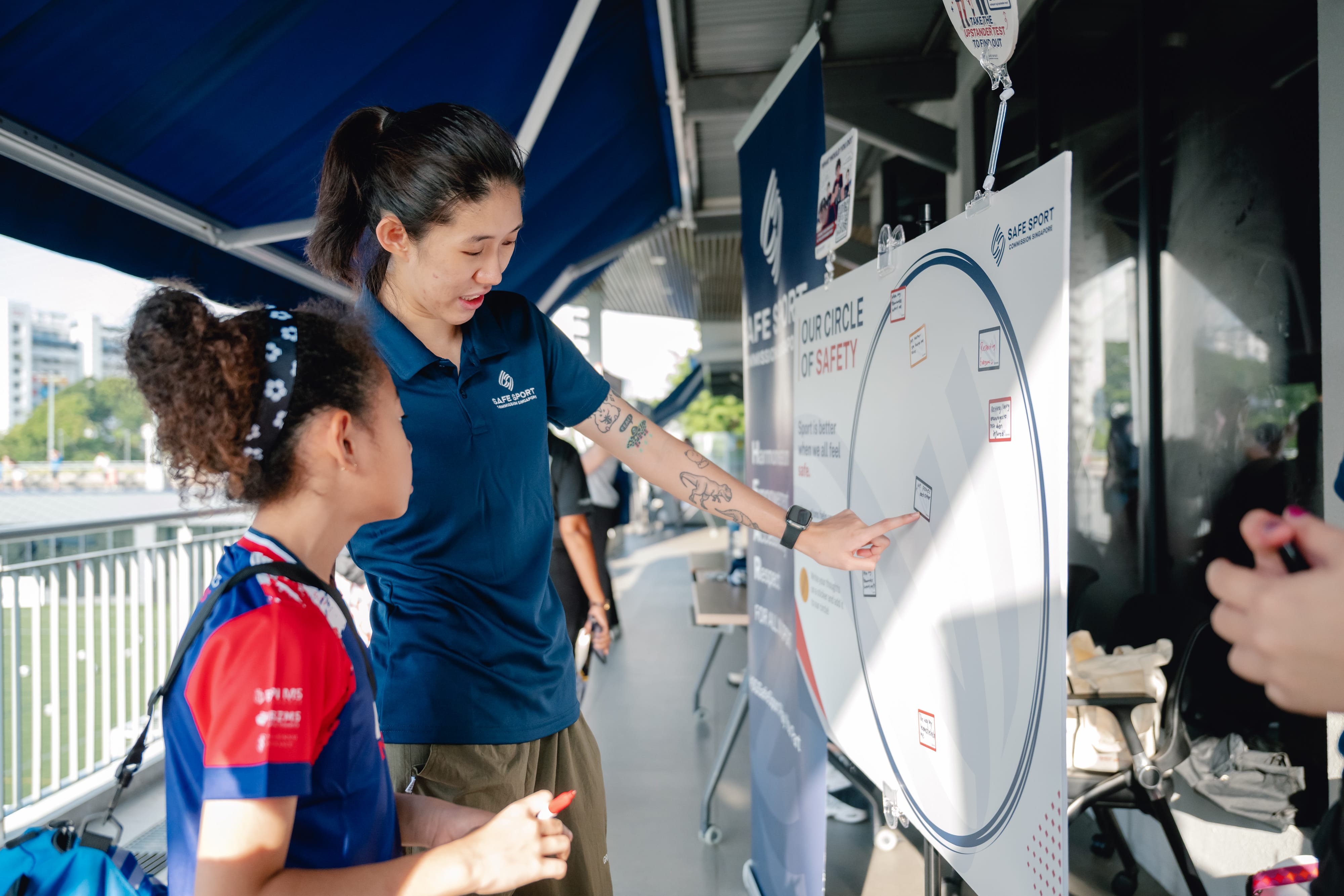 A woman and a young girl stand side by side, focused on a vibrant poster displayed in front of them.